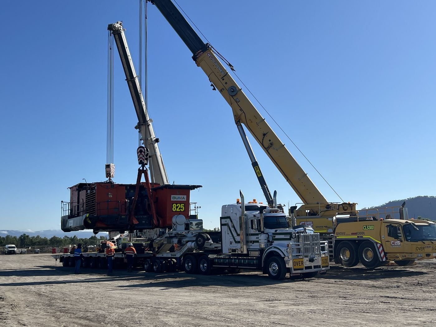 Two mobile cranes lifting a mining excavator house onto a low loader trailer