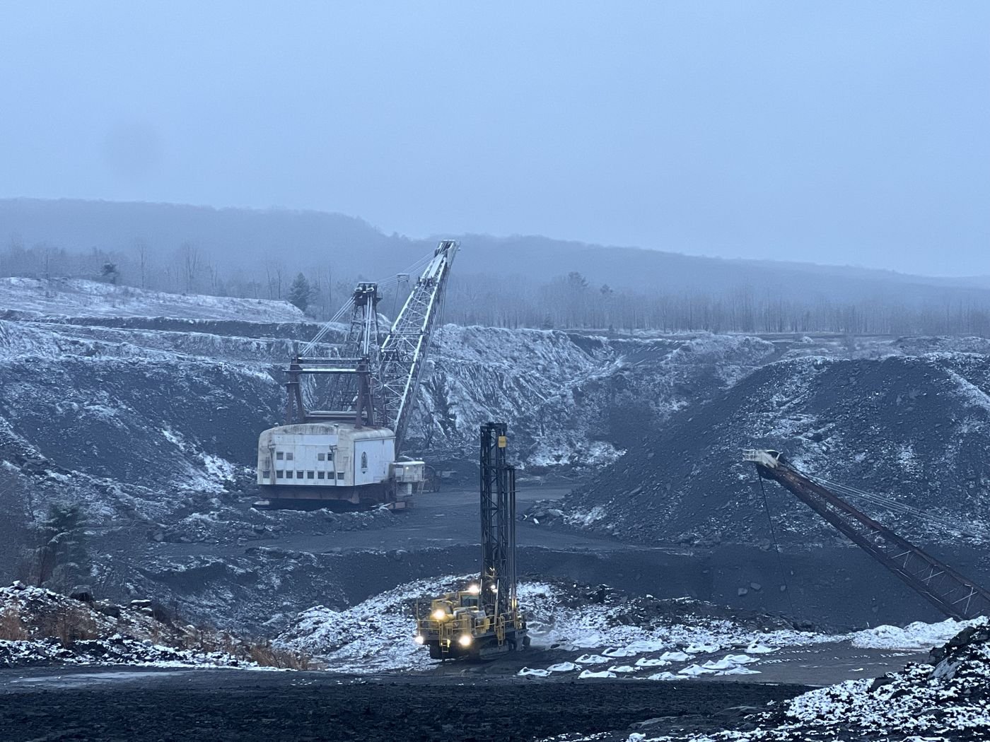 Walking dragline and a blast hole drill rig working a snow covered open cut coal pit
