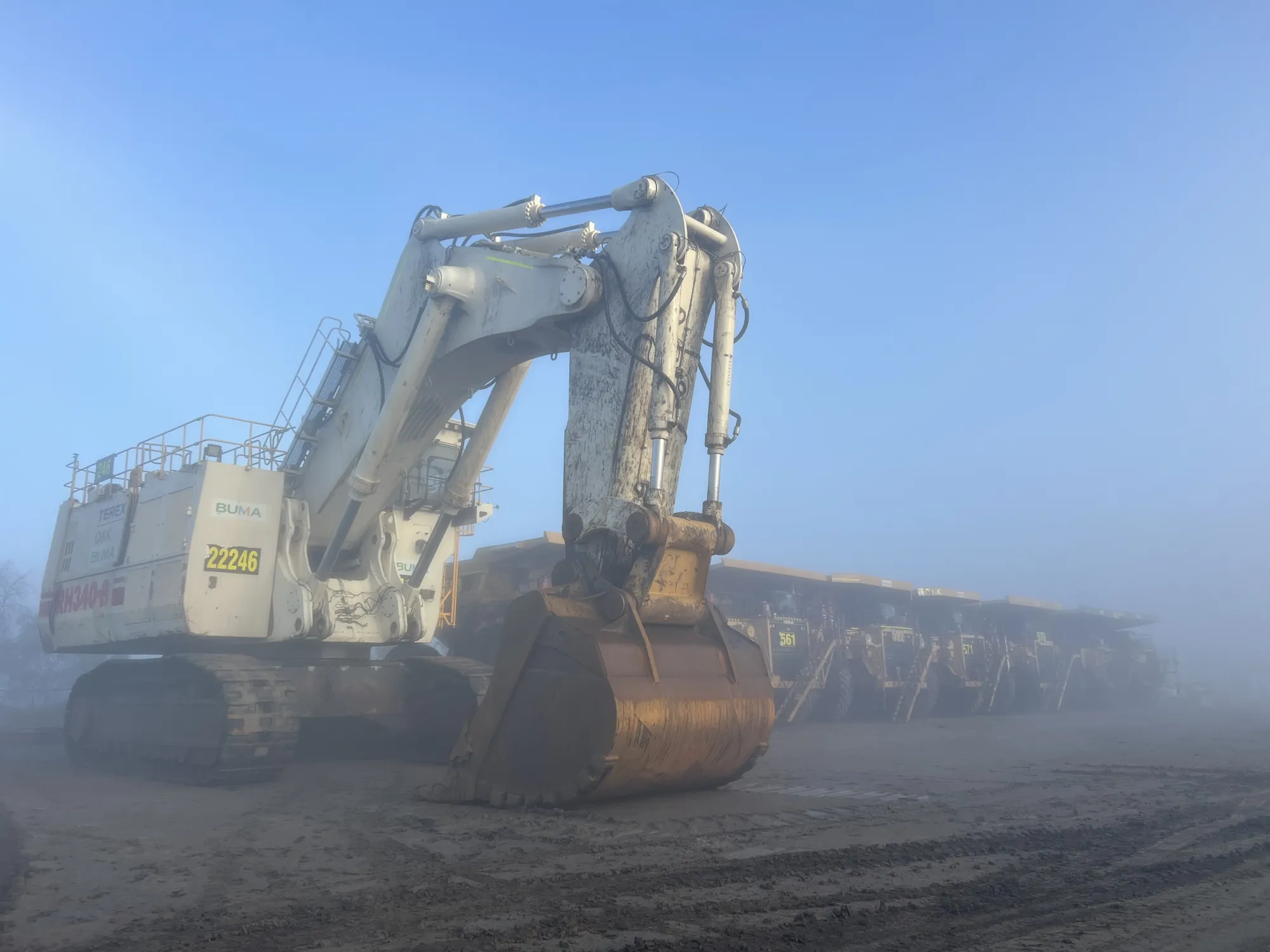 Liebherr mining excavator and haul trucks in early-morning fog on a coal mine site