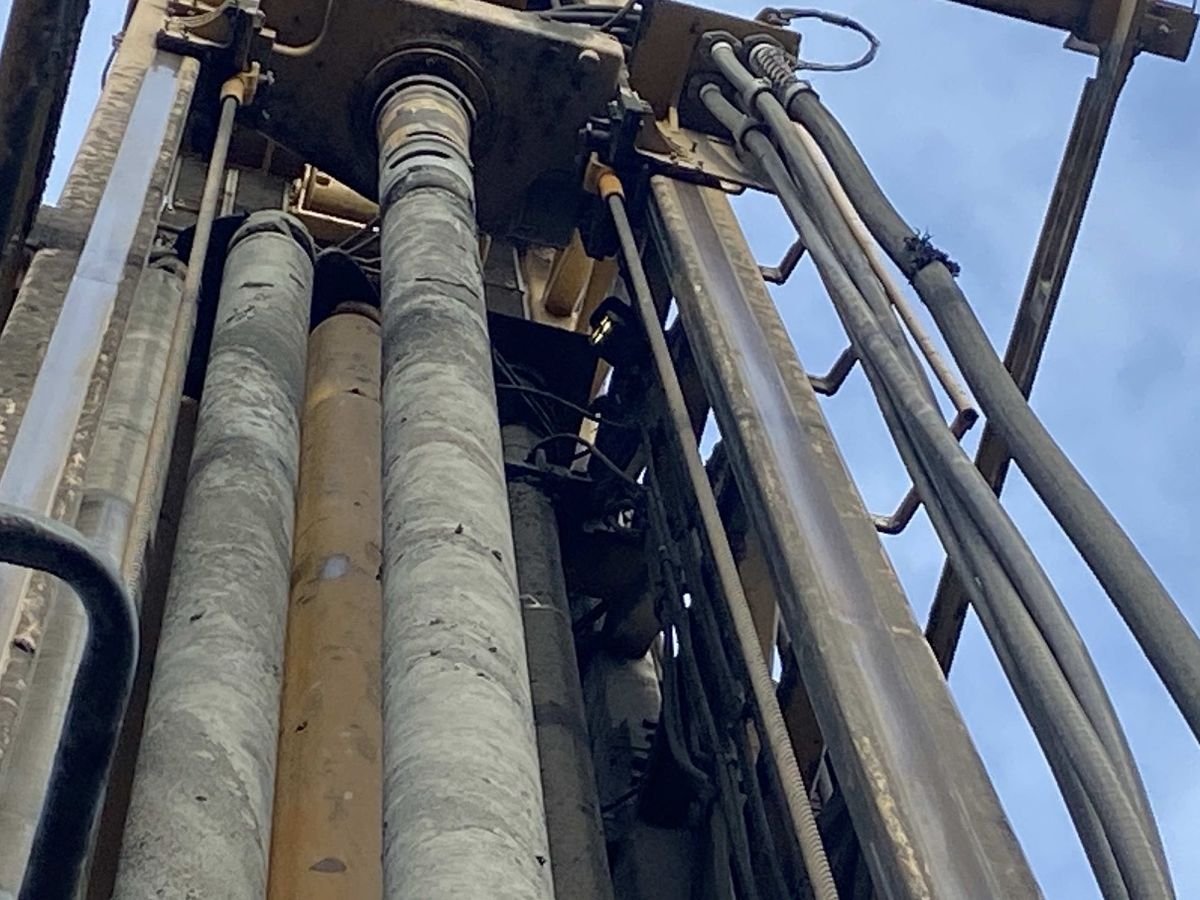 Hydraulic cylinders and hoses running up the mast of a drill rig on site
