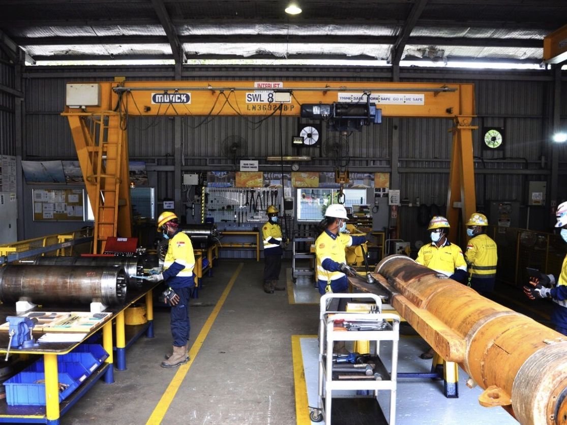 Maintenance crew in high visibility gear working on hydraulic cylinders under a gantry crane
